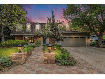 Charming brick home with a manicured lawn, a brick walkway, landscape lighting, and a two-car garage at dusk at 10158 E Fair Cir, Englewood, CO 80111