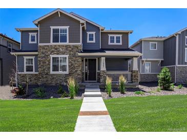 Inviting two-story home with stone accents, a covered porch, landscaped yard, and a well-manicured lawn at 11933 Norfolk Ct, Commerce City, CO 80022
