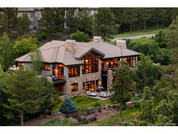 Expansive stone house featuring large windows and outdoor seating, nestled among lush trees at 786 International Isle Dr, Castle Rock, CO 80108