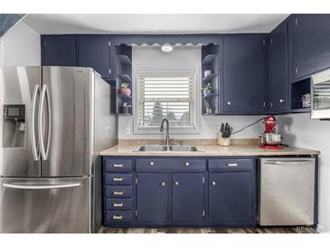 Cozy kitchen with navy cabinets, stainless steel appliances, and a double basin sink underneath a window at 7296 Quivas St, Denver, CO 80221
