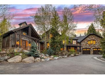 A luxurious stone and wood home with a circular driveway is framed by a vibrant sunset sky at 215 Royal Tiger Rd, Breckenridge, CO 80424