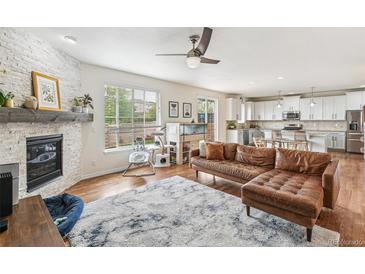 Spacious living room with a brick fireplace, ceiling fan, and a seamless transition to the modern kitchen at 24356 E Powers Ave, Aurora, CO 80016