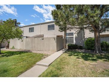 Charming townhome exterior with well-maintained lawn, trees, and concrete walkway to fenced entry at 7705 W 87Th Dr, Arvada, CO 80005