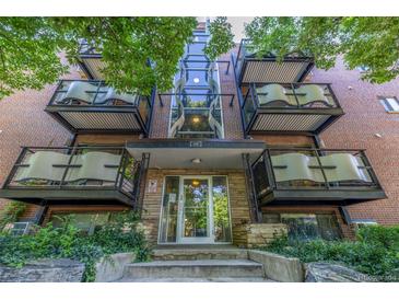 Brick apartment building featuring a glass-enclosed stairwell and balconies with green foliage in the front at 1245 Columbine St # 306, Denver, CO 80206