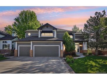 Charming two-story home featuring a three-car garage, manicured lawn, and lovely landscaping at sunset at 16342 Parkside Dr, Parker, CO 80134