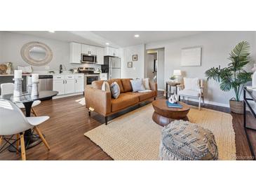 A comfortable living room featuring a modern brown sofa, area rug, and a view into the kitchen with stainless steel appliances at 1275 Winona Ct # B, Denver, CO 80204