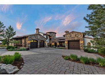 Stone home featuring a three-car garage and a circular entryway, complemented by manicured landscaping and a paved driveway at 7208 Raphael Ln, Littleton, CO 80125