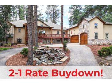 Beautiful home exterior featuring a stone facade, wood garage doors, deck, and water feature in a wooded setting at 4456 Mohawk Dr, Larkspur, CO 80118