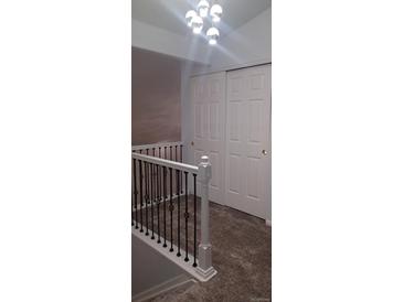 Hallway featuring new carpet, modern light fixture, closet, and white railing with dark spindles at 5319 Morning Glory Pl, Highlands Ranch, CO 80130