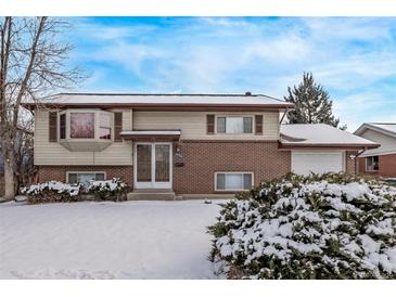 Charming two-story home featuring a brick facade and a cozy bay window, all dusted with a fresh layer of snow at 1520 Phillips Dr, Northglenn, CO 80233