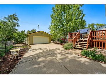 View of a backyard featuring a driveway, detached garage, and wooden deck with stairs leading up from the driveway at 5573 S Datura St, Littleton, CO 80120