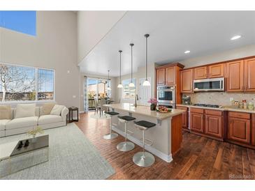 Bright kitchen and living room with hardwood floors, granite counters, island, and modern stainless-steel appliances at 15715 Carob Cir, Parker, CO 80134
