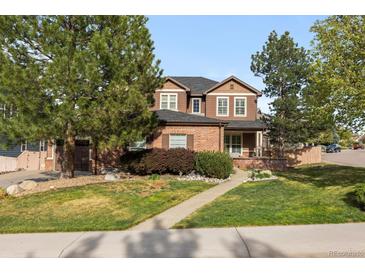 Charming two-story home features a brick facade, manicured lawn, and mature trees at 10700 Addison Ct, Highlands Ranch, CO 80126