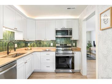 Stylish kitchen featuring white cabinetry, green backsplash, stainless steel appliances and butcher block counters at 1749 Havana St, Aurora, CO 80010