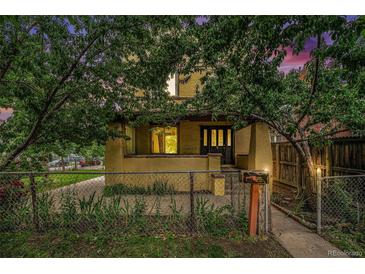 Charming two-story yellow home featuring a covered porch, mature trees, and fenced front yard at 7 Elati St, Denver, CO 80223