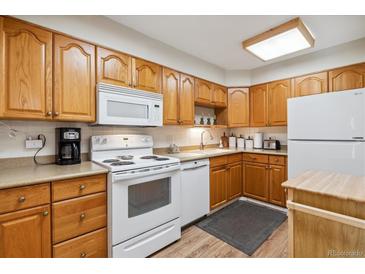 Traditional kitchen featuring wooden cabinets, white appliances, and a laminate countertop at 635 S Alton Way # 3B, Denver, CO 80247