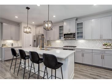 Modern kitchen features gray cabinets, stainless steel appliances, a central island with seating and pendant lighting at 431 Courtfield Way, Castle Pines, CO 80108