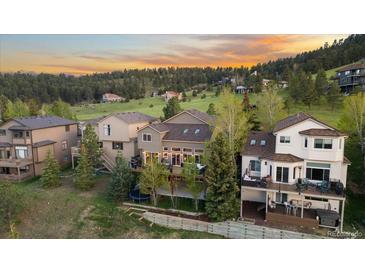 Gorgeous multi-level home with a lush green lawn nestled into a wooded hillside under an orange sunset at 24005 High Meadow Dr, Golden, CO 80401