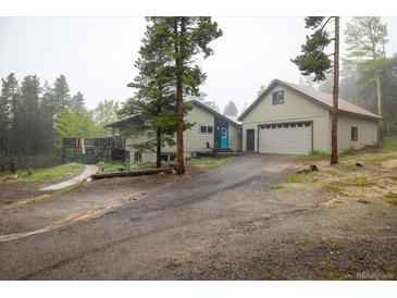 Charming home features a spacious driveway and an attached two-car garage nestled amongst mature pine trees at 1194 Camp Eden Rd, Golden, CO 80403