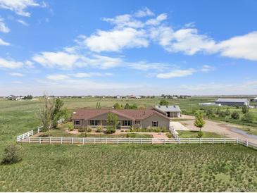 Sprawling ranch-style home with white fence on a lush, open lot and a detached garage on a sunny day at 32501 E 137Th Way, Brighton, CO 80603