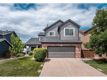 Charming two-story home featuring gray siding, brick accents, a well-manicured lawn, and an attached two-car garage at 9758 Red Oakes Dr, Highlands Ranch, CO 80126