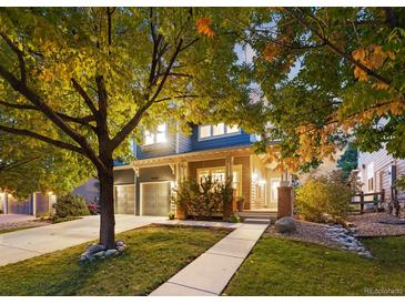 Charming two-story home with a well-manicured lawn, mature trees, and covered front porch at 16456 Wagon Pl, Parker, CO 80134