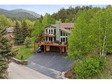 Stunning view of a multi-level home with decks, a driveway, mature trees, and mountain scenery at 4230 S Meadow Brook Ln, Evergreen, CO 80439