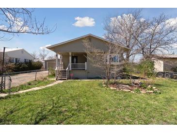 Charming single-story home with a front porch, green lawn, and a chain-link fence at 575 2Nd St, Bennett, CO 80102