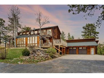 Stunning multi-level home with a two-car garage and beautiful wood siding, complemented by lush greenery at 13660 Rampart Dr, Conifer, CO 80433