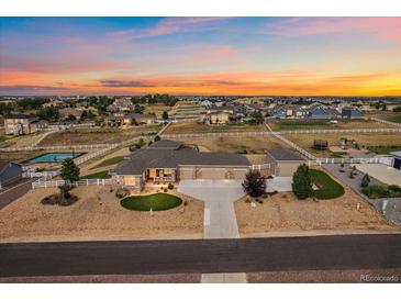Expansive aerial view of a ranch home with manicured landscaping, outbuildings, and fenced yard at sunset at 12590 Valentia St, Thornton, CO 80602
