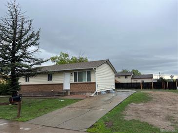 Cozy single-story home with a brick foundation, concrete driveway, and spacious front yard, perfect for outdoor activities at 405 Dogwood Ave, Brighton, CO 80601