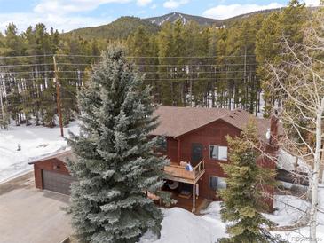 Mountain home featuring a large yard, balcony, and a two-car garage nestled amongst mature trees in a picturesque mountain landscape at 9239 Black Mountain Dr, Conifer, CO 80433