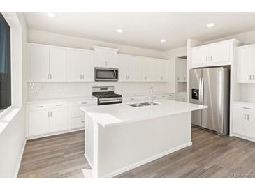 Bright kitchen featuring white cabinets, stainless steel appliances, large island, and stylish backsplash at 9089 Pitkin St, Commerce City, CO 80022