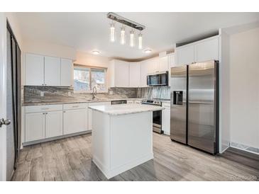 Bright kitchen with gray floors, white cabinets, stainless steel refrigerator, and stone countertops at 1832 Simms St, Lakewood, CO 80215