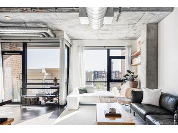 Bright living room features exposed concrete, industrial ductwork, and city views from black framed windows at 2100 16Th St # 405, Denver, CO 80202