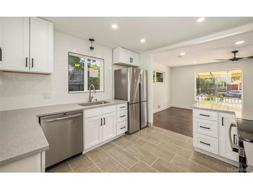 Bright kitchen boasts stainless steel appliances, white cabinetry, quartz countertops and modern tile flooring at 7691 Osage St, Denver, CO 80221