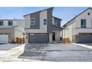 Modern two-story home with gray siding, a gray garage door, and a concrete driveway partially covered in snow at 19088 E 94Th Pl, Commerce City, CO 80022