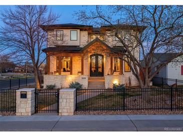 Elegant two-story home boasts stone accents, a covered front porch with wooden columns, and a beautifully landscaped yard with iron fence at 2600 S Adams St, Denver, CO 80210