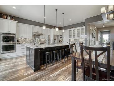 Spacious kitchen with white cabinets, dark island, granite countertops, and wood floors at 15804 Elizabeth E Cir, Thornton, CO 80602