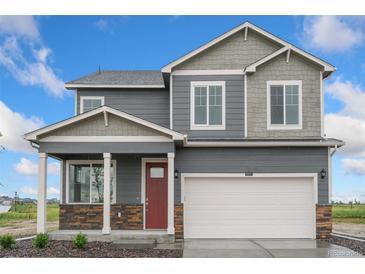 Two-story home featuring gray siding, stone accents, a red front door, and a two-car garage at 4757 Windmill Dr, Brighton, CO 80601