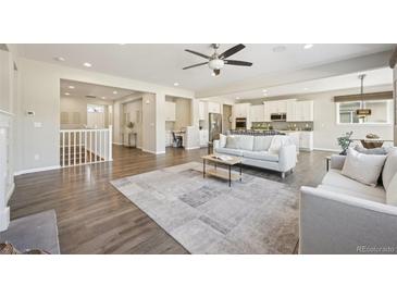 Spacious living room with hardwood floors, neutral decor, and seamless flow to the kitchen at 15993 E 112 Pl, Commerce City, CO 80022