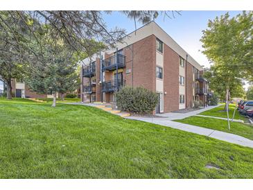 A well-kept three-story brick apartment building with green grass and mature trees in a beautiful park-like setting at 5995 W Hampden Ave # 17F, Denver, CO 80227