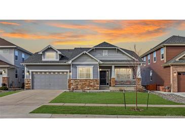 Charming two-story home with stone accents, manicured lawn, and an inviting covered front porch at sunset at 20795 Scenic Park Dr, Parker, CO 80138
