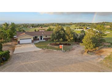 Scenic view of a tan ranch home, landscaped front yard, attached garage, and expansive fields with a rainbow in the background at 3850 Hopi Dr, Sedalia, CO 80135