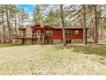Charming wood-sided home featuring a stone chimney and a spacious deck surrounded by lush trees at 1150 Fremont Dr, Larkspur, CO 80118