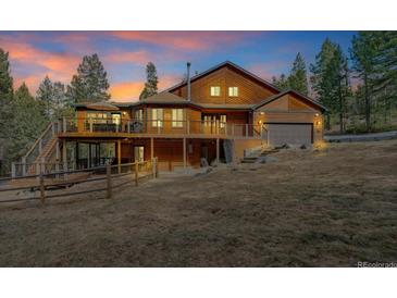 Two-story wood home with a deck, garage, and lush surrounding trees under a stunning sunset sky at 9590 S Warhawk Rd, Conifer, CO 80433