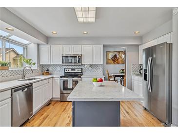 Modern kitchen with stainless steel appliances, white cabinetry, and large island with quartz countertops at 12551 W 84Th Cir, Arvada, CO 80005