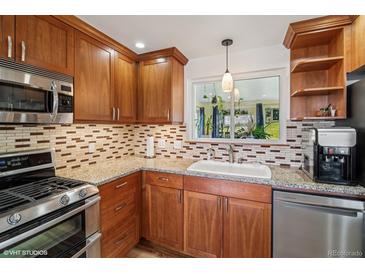 Modern kitchen with stainless steel appliances, granite countertops, wood cabinetry, and natural light from window at 11600 W 31St Pl, Lakewood, CO 80215