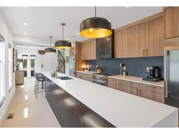 Modern kitchen boasts a long center island, sleek countertops, stylish pendant lights, and stainless steel appliances at 2702 Lowell Blvd, Denver, CO 80211
