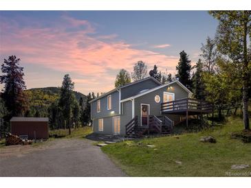 Charming two-story home with a deck and rustic accents nestled among tall trees at sunset at 32252 Steven Way, Conifer, CO 80433